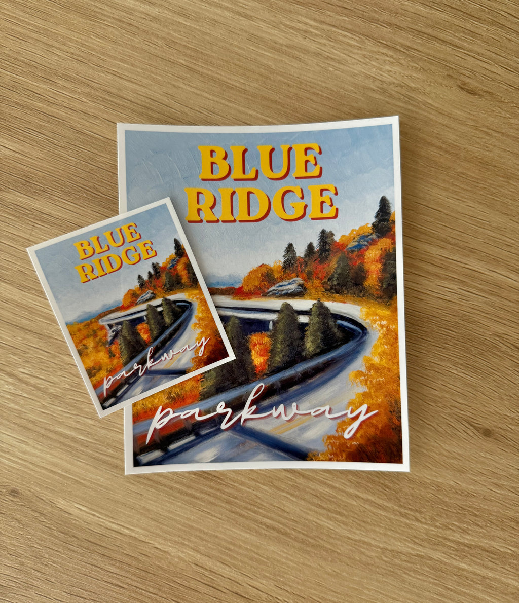 Two stickers featuring a scenic autumn landscape labeled "BLUE RIDGE" and "parkway," placed on a light wood surface.