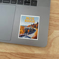 A rectangular sticker with a white border featuring an autumn landscape illustration and the text 'BLUE RIDGE' and 'parkway', placed on the palm rest of a silver laptop on a wooden surface.