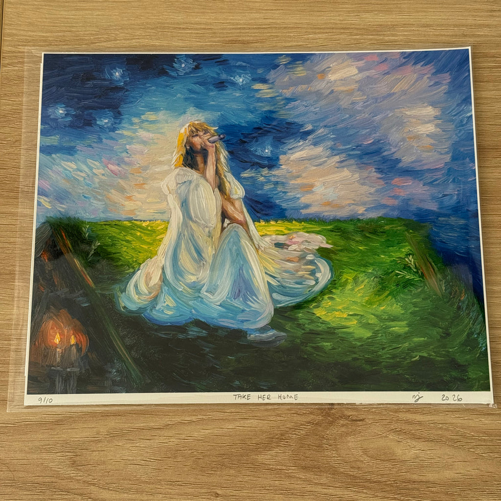 An art print of a painting titled 'TAKE HER HOME' displayed on a light wood floor. The painting depicts a woman in a flowing white gown sitting in a grassy field under a starry night sky, with a small set of candles burning in the background.