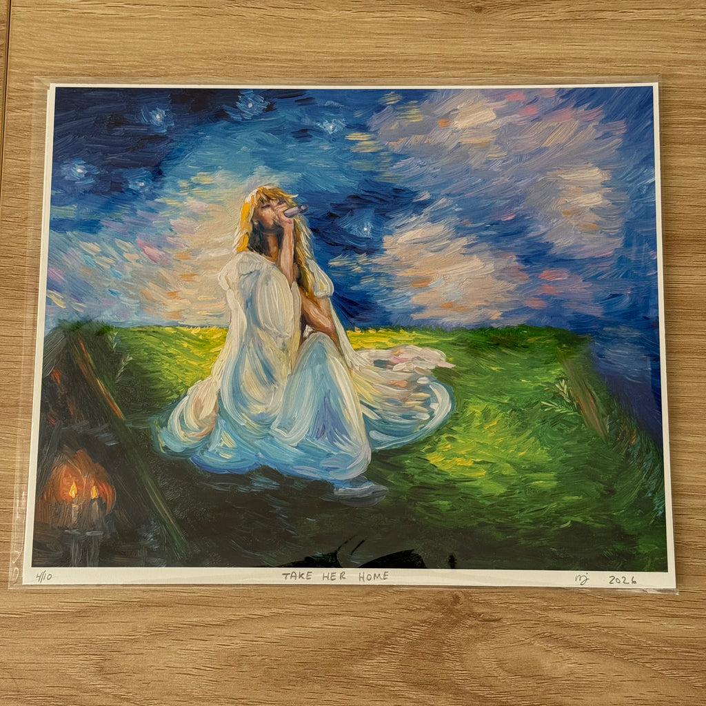 An art print of a painting titled 'TAKE HER HOME' displayed on a light wood floor. The painting depicts a woman in a flowing white gown sitting in a grassy field under a starry night sky, with a small set of candles burning in the background.