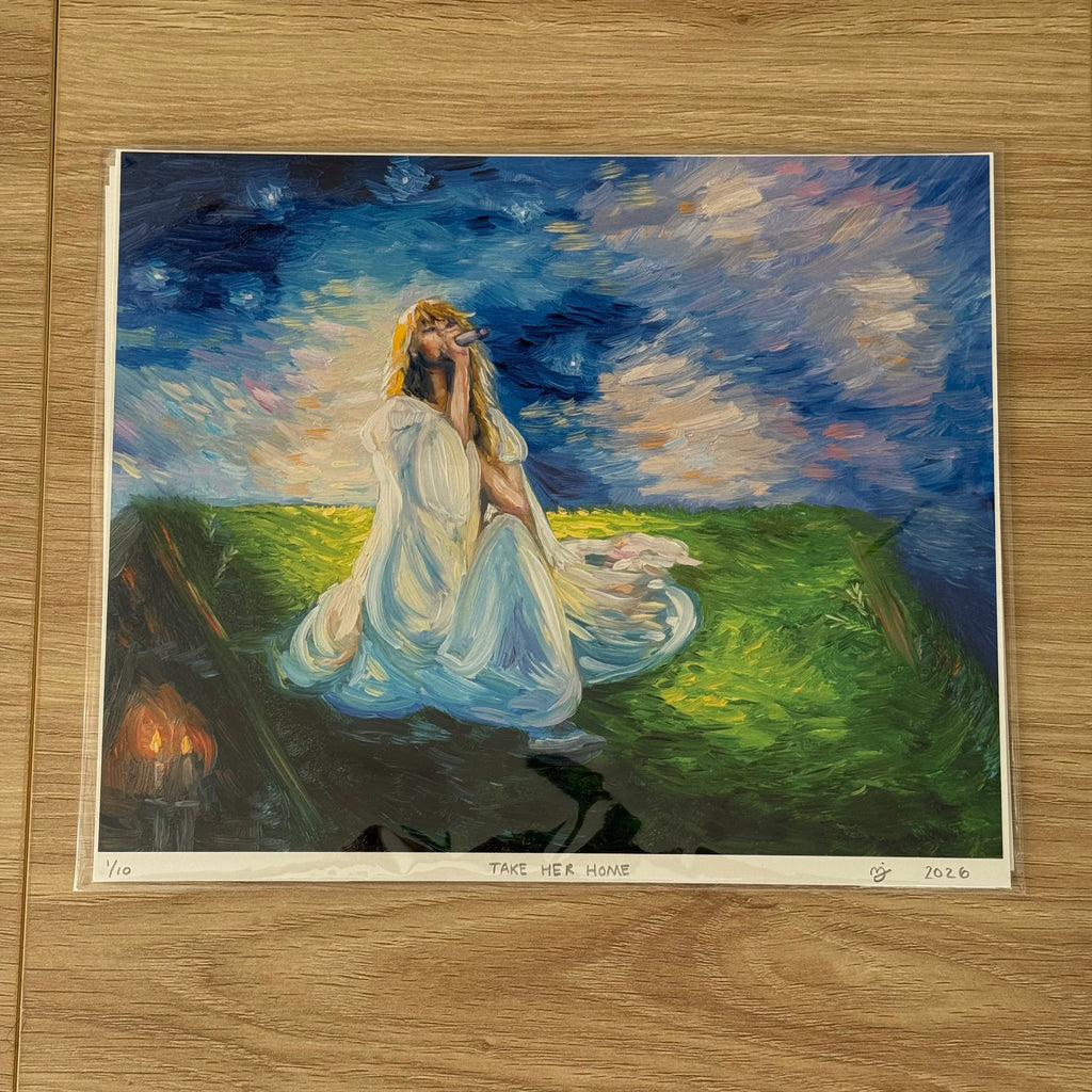 An art print of a painting titled 'TAKE HER HOME' displayed on a light wood floor. The painting depicts a woman in a flowing white gown sitting in a grassy field under a starry night sky, with a small set of candles burning in the background.