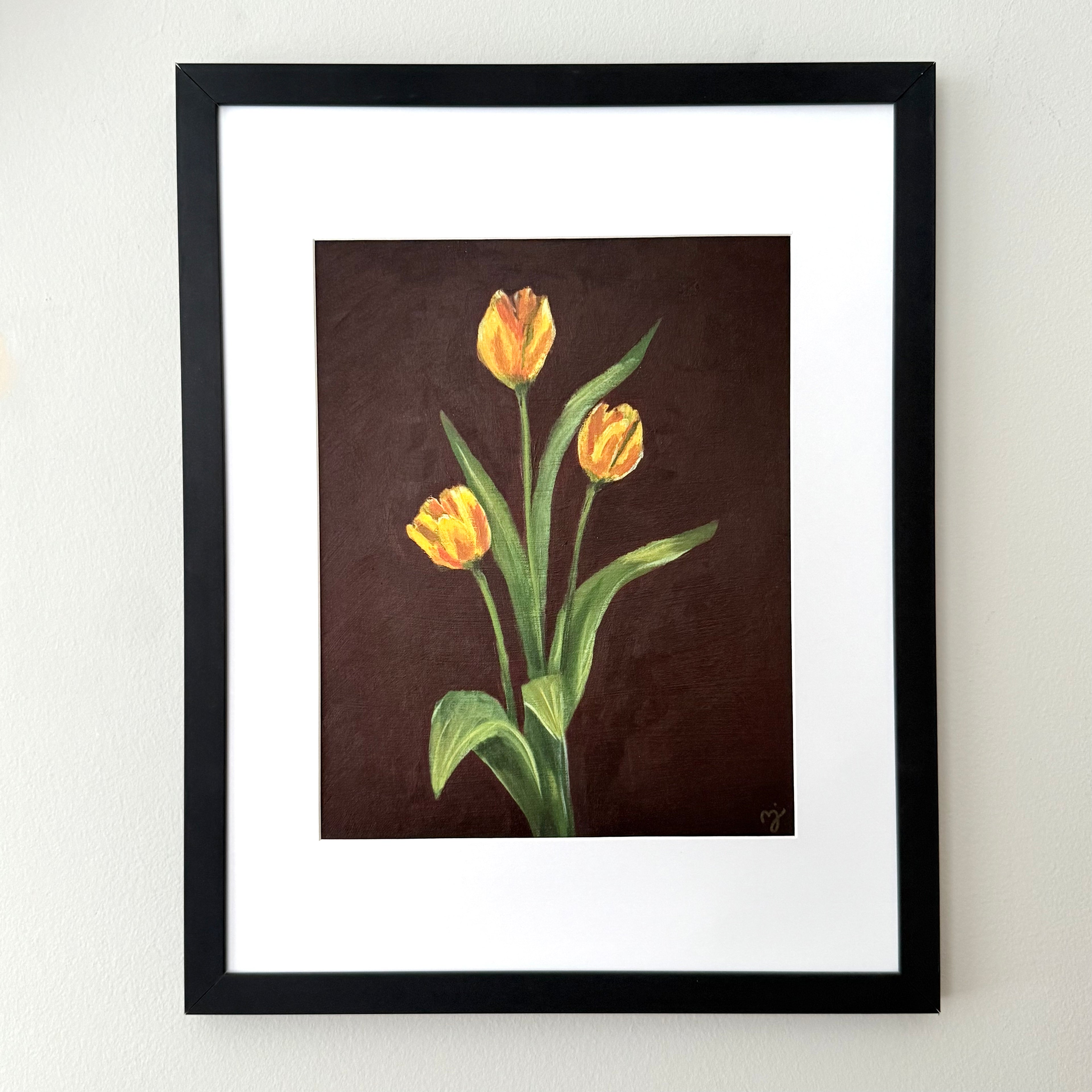 Framed floral wall art featuring three yellow tulips on a dark brown background, mounted with a white mat and a black frame on a light wall.