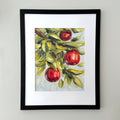 A framed art print featuring a painted still life of three red apples on a branch with green and yellow leaves, set against a light gray wall.