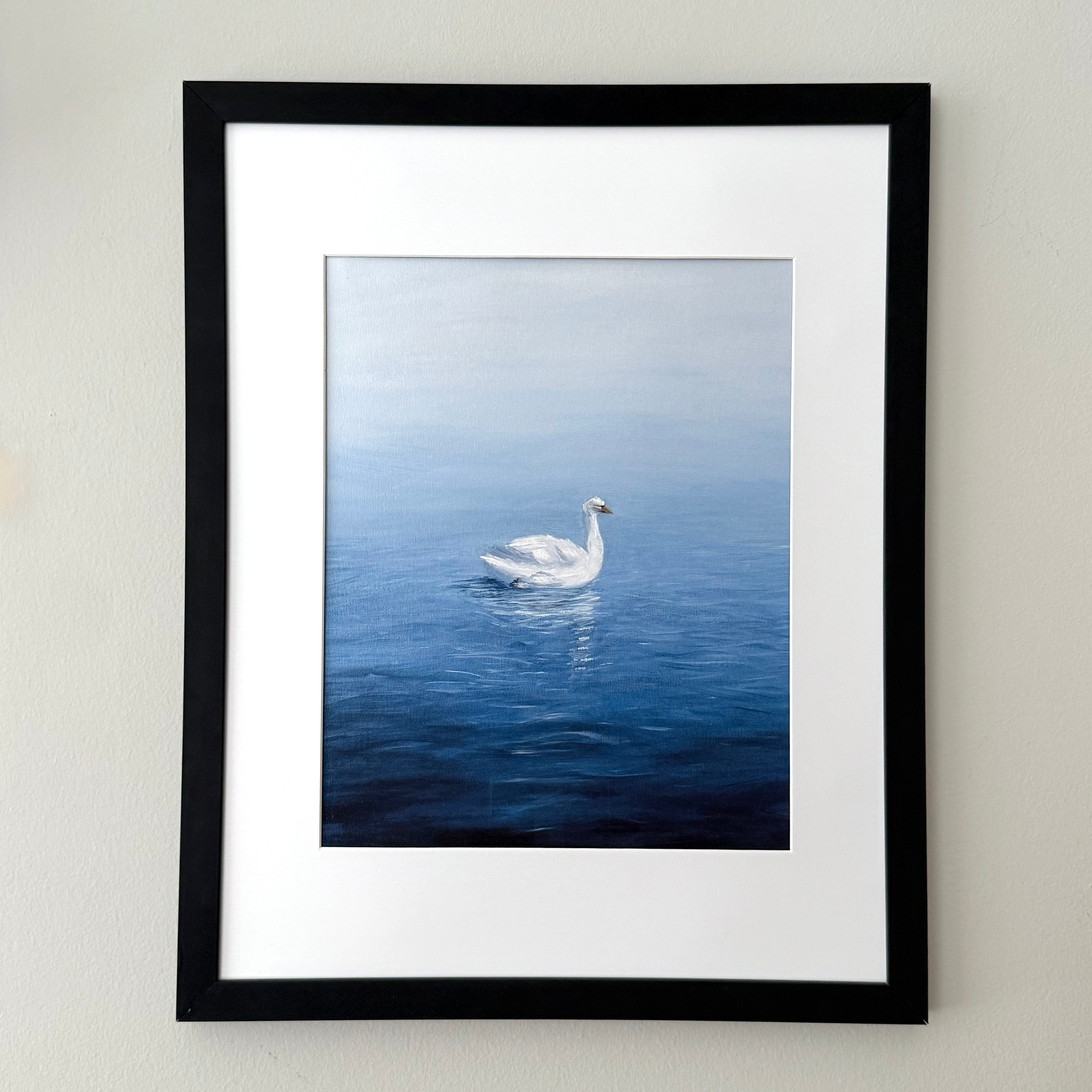 Framed wall art featuring a painting of a white swan on deep blue water, with a white mat and a black frame, mounted on a light beige wall.