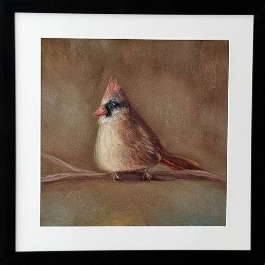A framed art print featuring a painted cardinal perched on a branch, displayed on a light gray wall. The artwork has a brown and beige background with the cardinal in brown, beige, and red tones, surrounded by a white mat and a black frame.