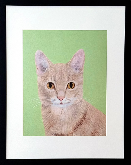 A framed art print featuring a portrait of an orange tabby cat on a light green background, housed in a black frame with a white mat, mounted on a beige wall.