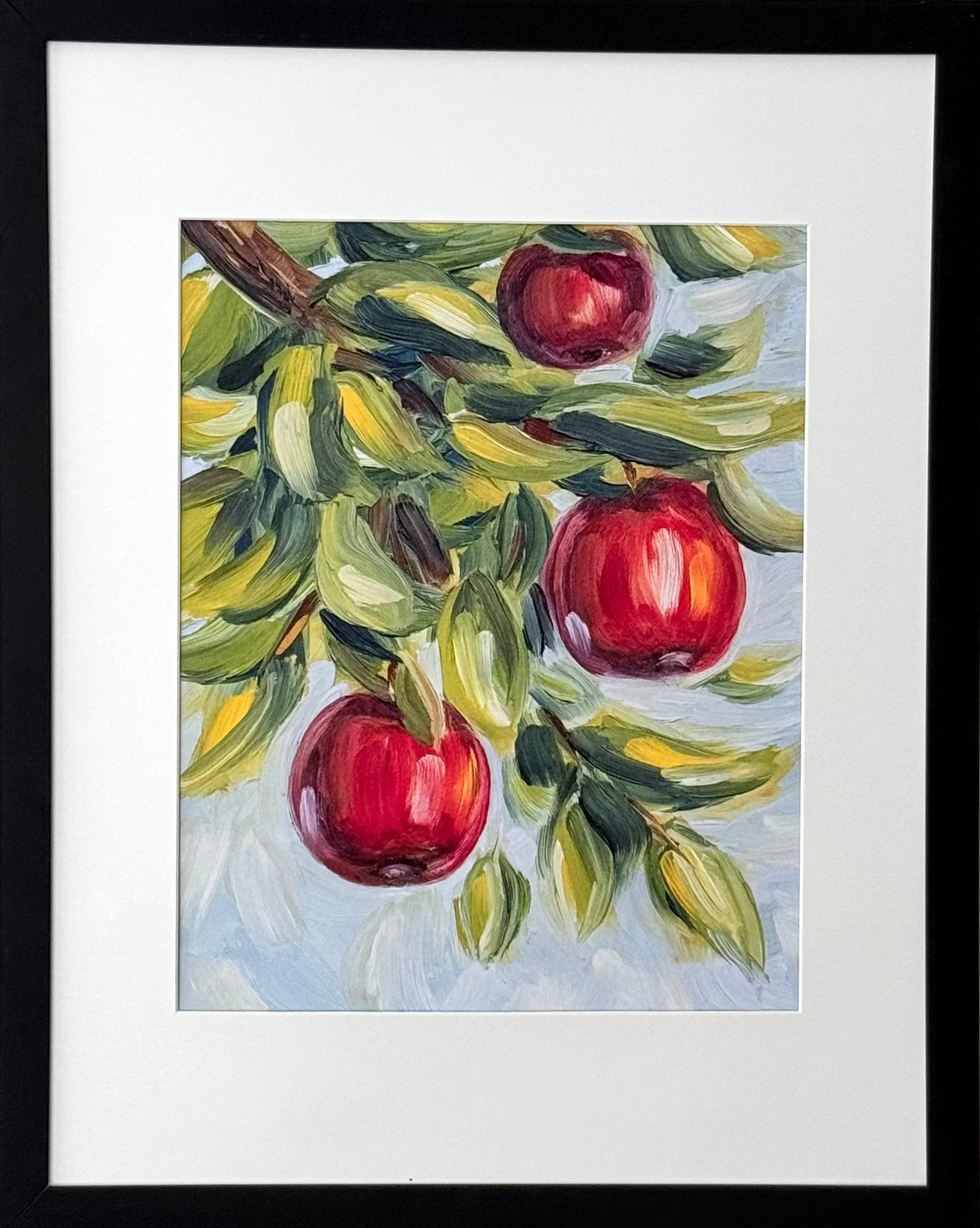 Framed wall art featuring a painted apple branch with three red apples, mounted on a light neutral wall.