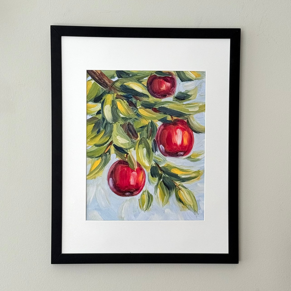 Framed wall art featuring a painted apple branch with three red apples, mounted on a light neutral wall.