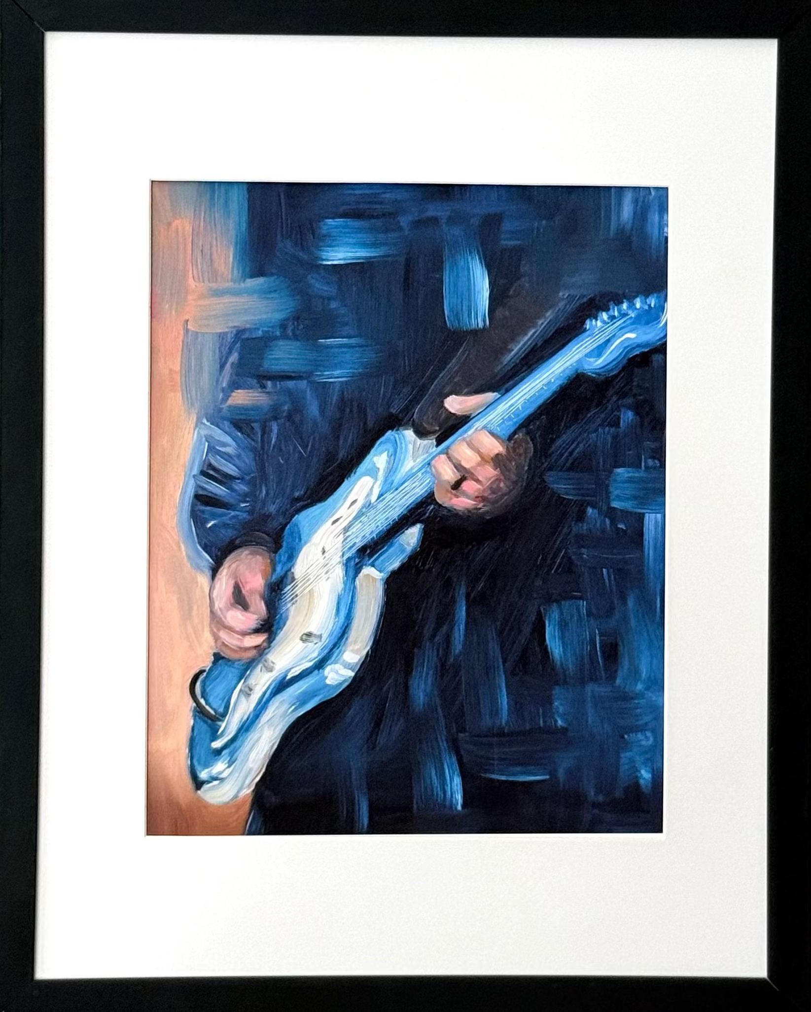 A framed art print featuring an expressive blue painting of a person playing an electric guitar, mounted on a light beige wall.