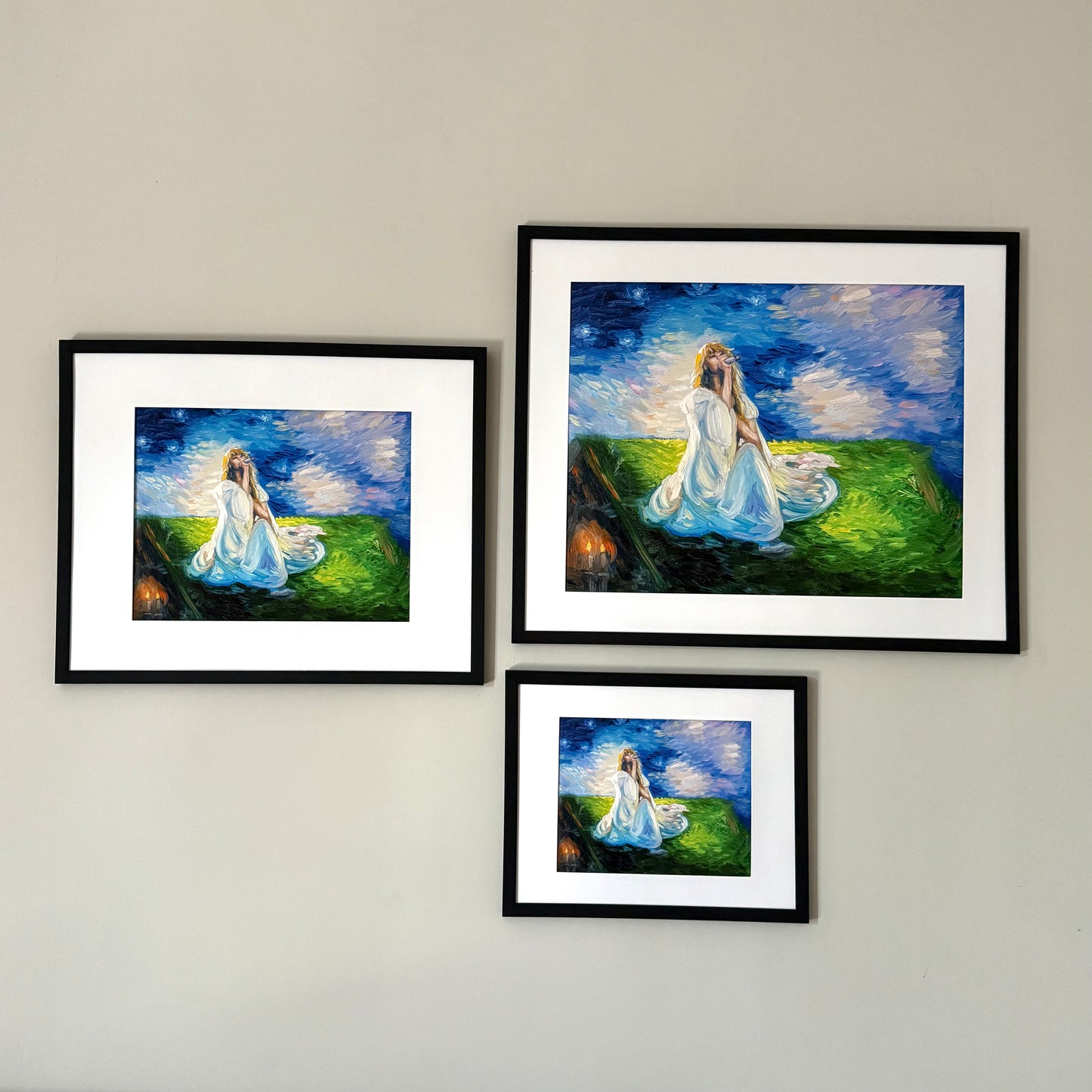 Three framed prints in various sizes of a blonde woman sitting in the grass holding a microphone with a starry blue background.