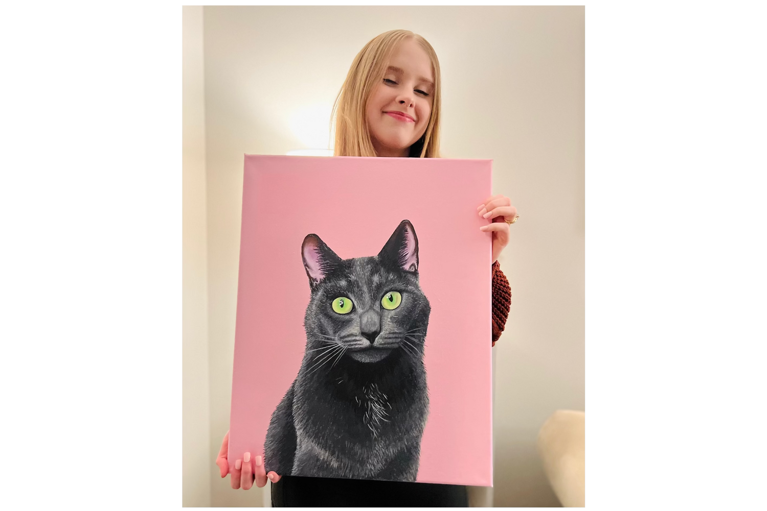 Person holding a painting of a gray cat with green eyes on a pink background