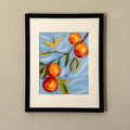 Print of a painting of an orange tree branch in a black frame against a white wall