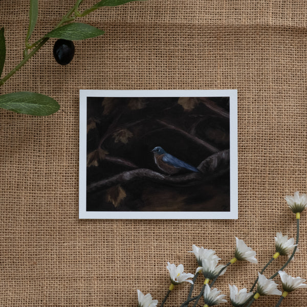 Burlap background with various floral decorations surrounding a fine art print depicting a bluebird sitting on a branch with a brown background