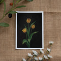Burlap background with various floral decorations surrounding a fine art print depicting 3 yellow tulips on a brown background
