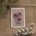 Burlap background with various floral decorations surrounding a fine art print depicting pink roses on a yellow background