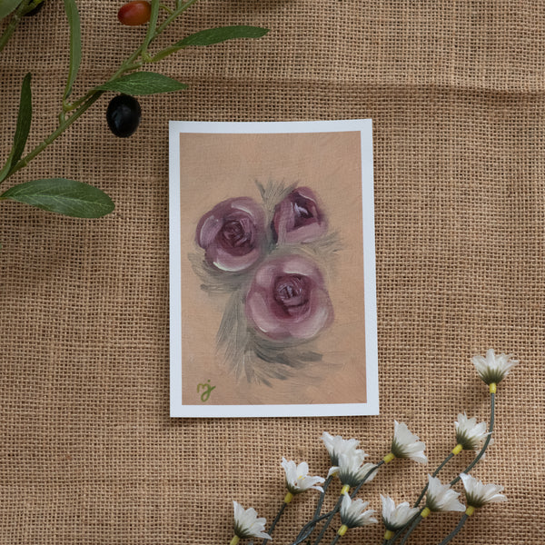 Burlap background with various floral decorations surrounding a fine art print depicting pink roses on a yellow background