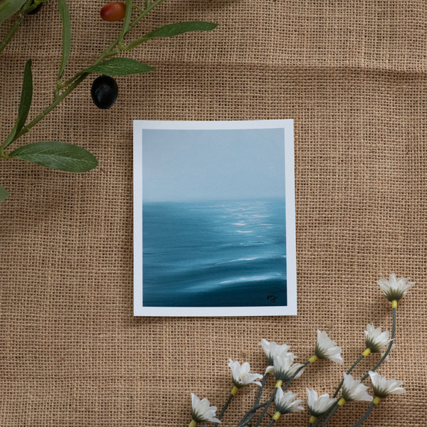 Burlap background with various floral decorations surrounding a fine art print depicting blue ocean waves with sun reflections and a light blue sky