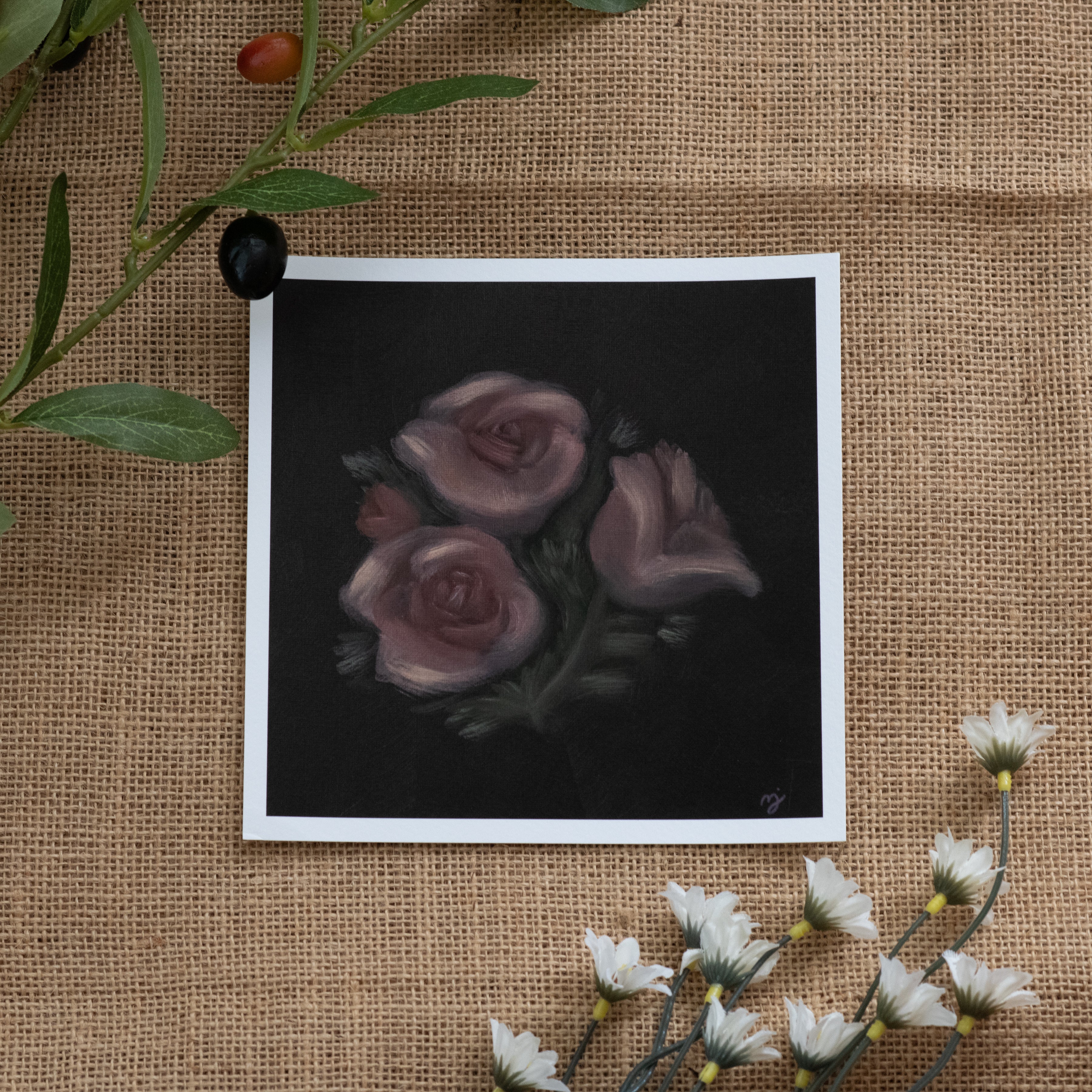Burlap background with various floral decorations surrounding a fine art print depicting pink roses on a brown background