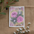 Burlap background with various floral decorations surrounding a fine art print depicting pink roses on a yellow background