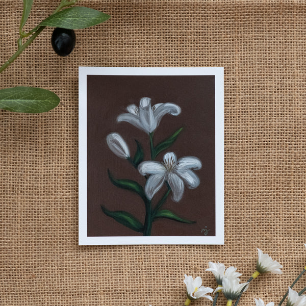 Burlap background with various floral decorations surrounding a fine art print depicting white lilies on a brown background