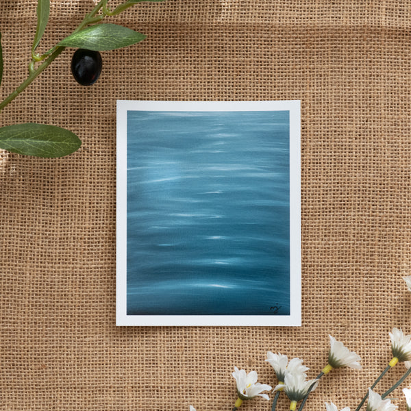 Burlap background with various floral decorations surrounding a fine art print depicting blue ocean waves with sun reflections