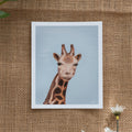 Burlap background with various floral decorations surrounding a fine art print depicting a giraffe's head and neck against a blue sky