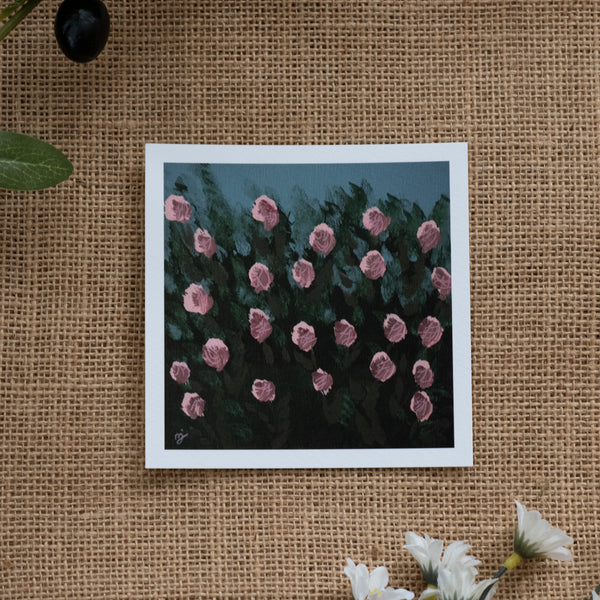 Burlap background with various floral decorations surrounding a fine art print depicting a bunch of pink roses and green shrubbery with a blue sky