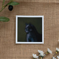 Burlap background with various floral decorations surrounding a fine art print depicting a dark grey cat against a green background